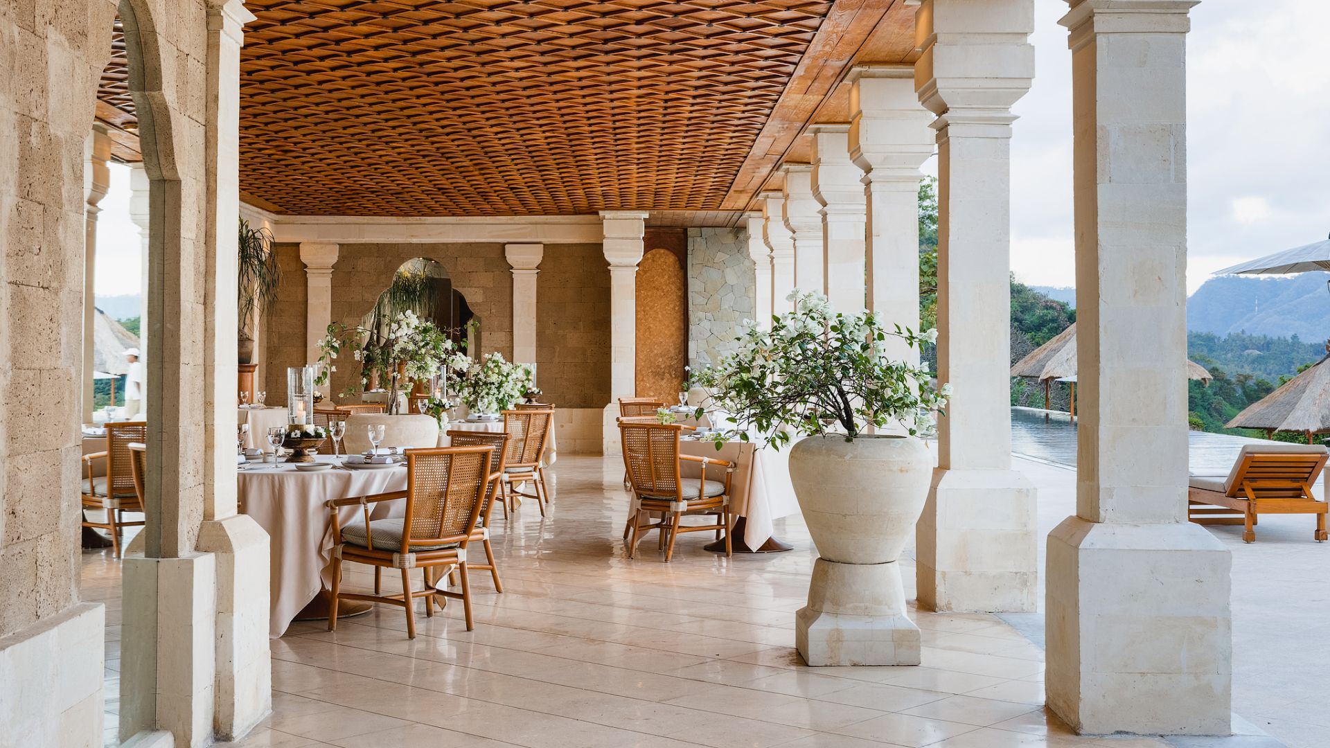 The open-sided restaurant at Amankila, set with tables under a woven wooden ceiling overlooking the pool