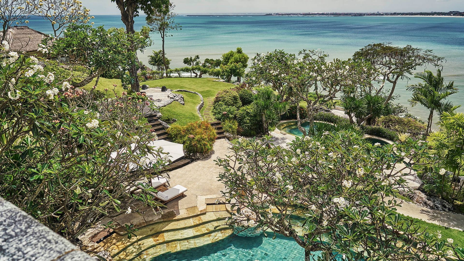 Aerial view of the gardens and pools at Four Seasons Resort Bali at Jimbaran Bay, framed by frangipani trees