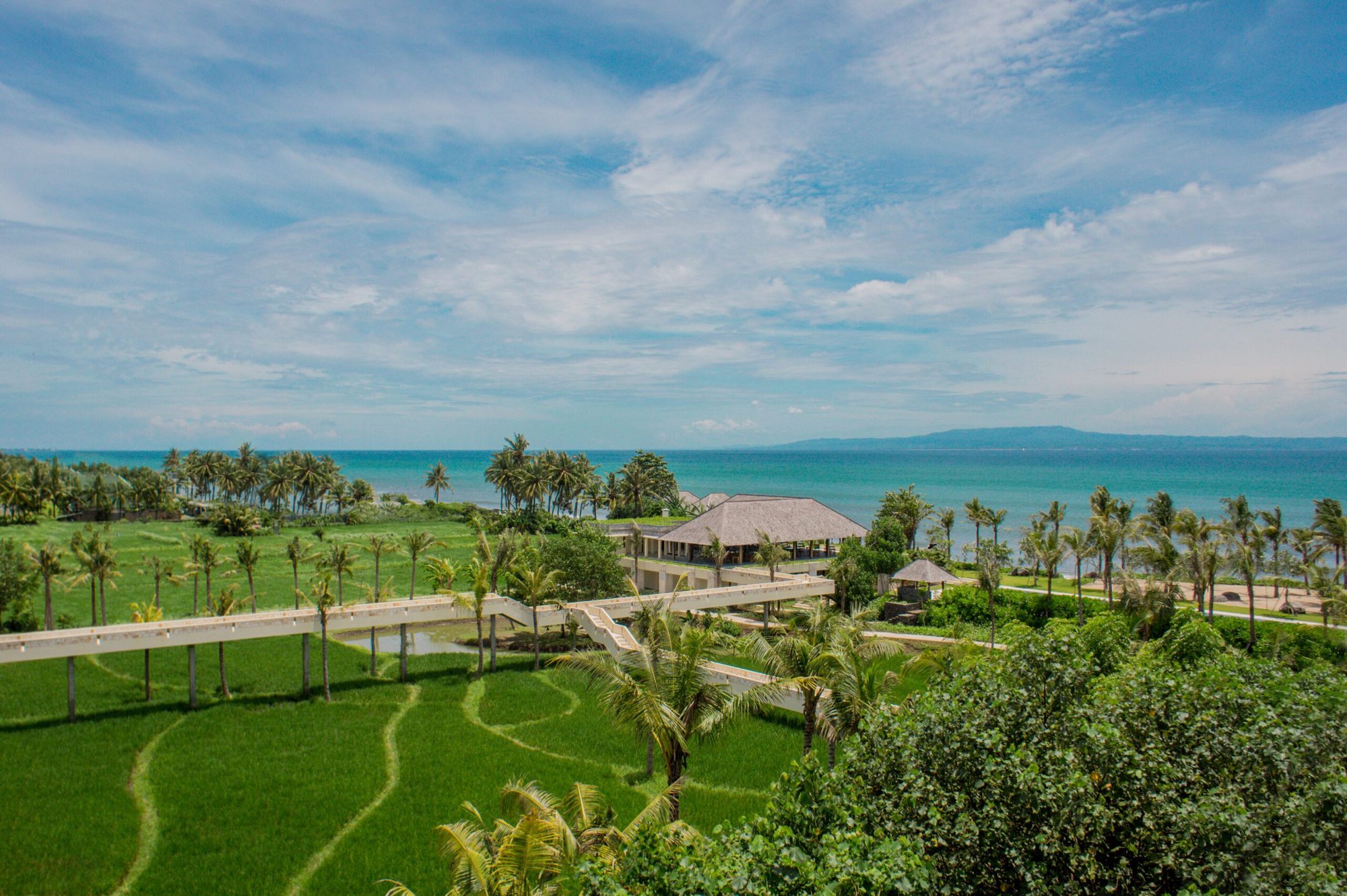 Raised walkways crossing living rice fields at Komaneka at Keramas Beach, leading toward the ocean