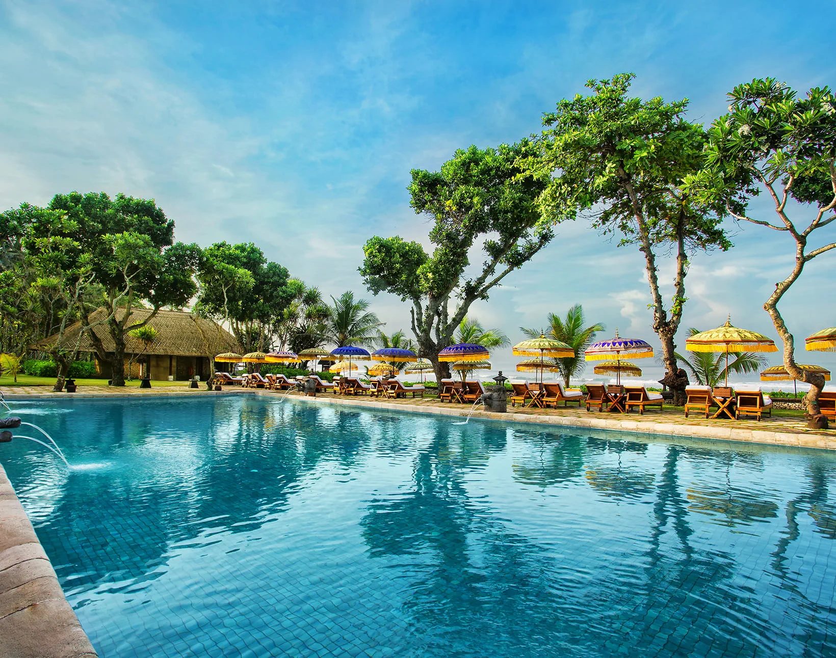 Poolside loungers and Balinese umbrellas at The Oberoi Bali, with the ocean beyond